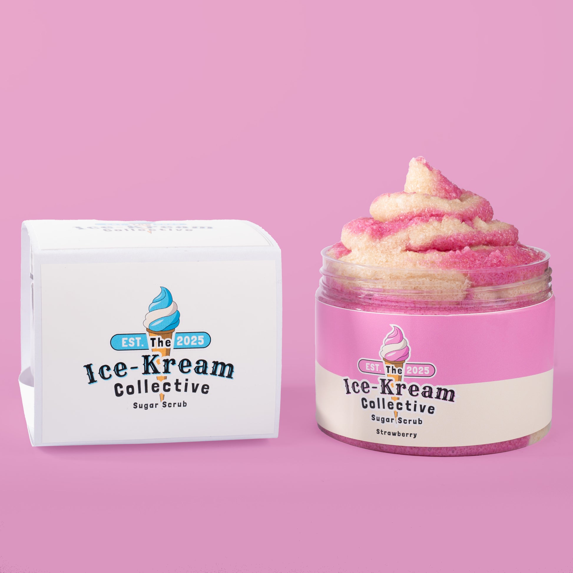 The Ice-Kream Collective Strawberry sugar scrub in a clear jar with pink and cream packaging, displayed next to its branded box on a pastel pink background.
